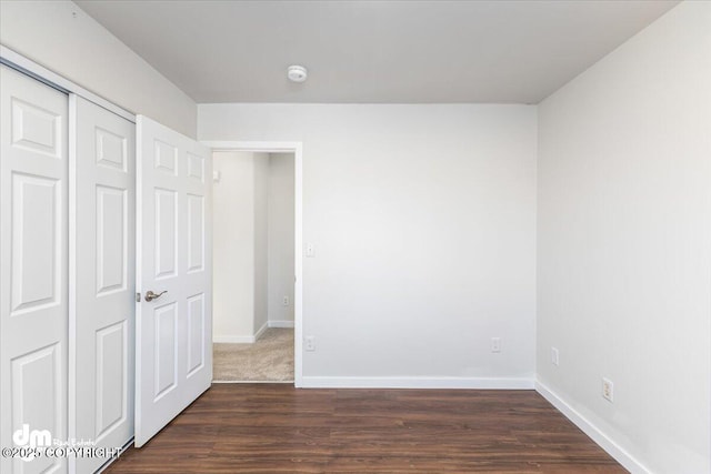 unfurnished bedroom featuring dark wood-type flooring, a closet, and baseboards