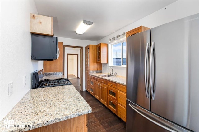 kitchen with light stone counters, dark wood-type flooring, a sink, appliances with stainless steel finishes, and brown cabinets