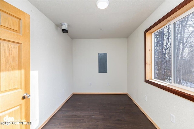 unfurnished room featuring electric panel, baseboards, and dark wood finished floors