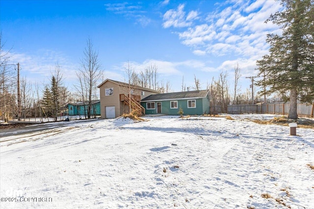 snow covered property with an attached garage and fence