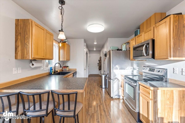 kitchen with dark countertops, light wood finished floors, a peninsula, stainless steel appliances, and a sink