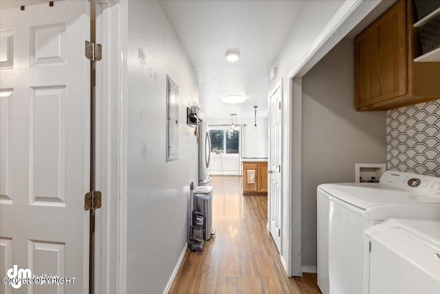 clothes washing area with washing machine and clothes dryer, cabinet space, baseboards, and light wood-style floors