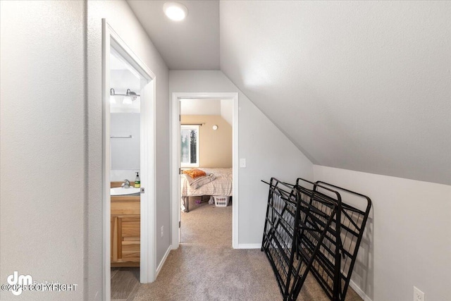 hallway featuring vaulted ceiling, a sink, baseboards, and carpet floors