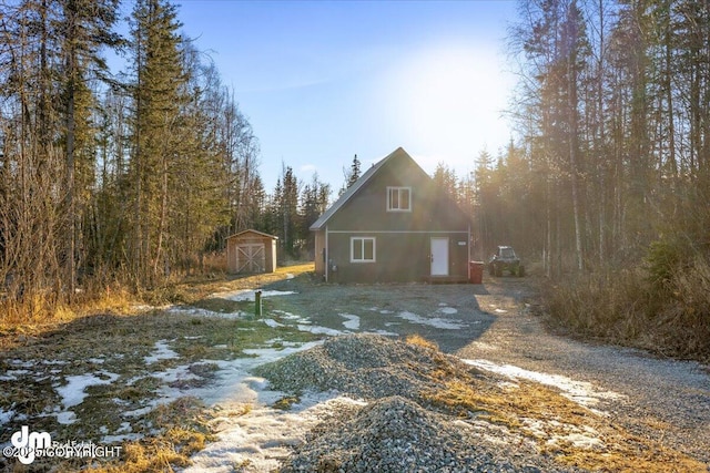 rear view of property with a storage shed, an outbuilding, gravel driveway, and stucco siding