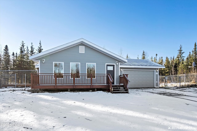 snow covered house featuring a deck, an attached garage, and fence