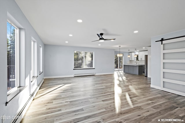 unfurnished living room featuring a barn door, a wealth of natural light, and a baseboard radiator