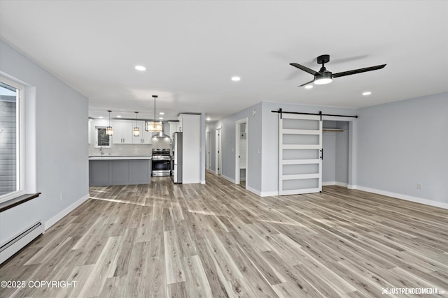 unfurnished living room featuring ceiling fan, light wood-type flooring, a baseboard heating unit, and a barn door