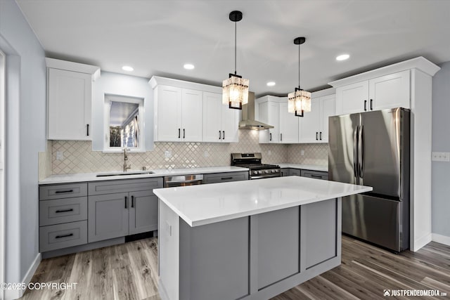 kitchen featuring gray cabinetry, a sink, stainless steel appliances, wall chimney exhaust hood, and light countertops