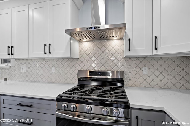 kitchen featuring wall chimney exhaust hood, stainless steel range with gas stovetop, backsplash, and gray cabinetry