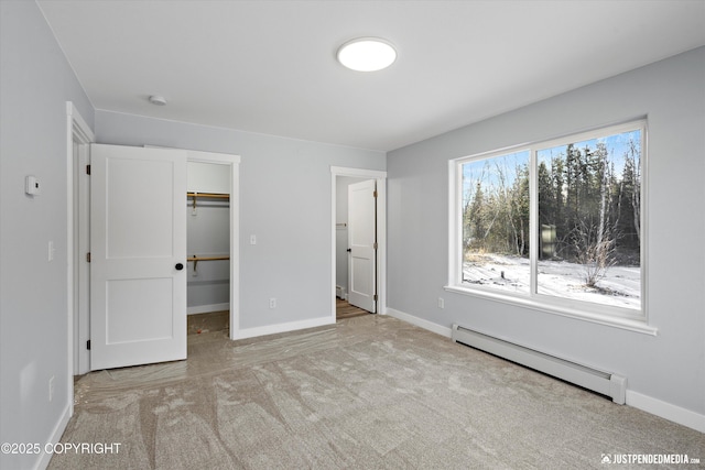 unfurnished bedroom with a spacious closet, a baseboard heating unit, baseboards, carpet, and a closet