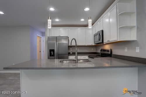 kitchen with a peninsula, open shelves, recessed lighting, a sink, and appliances with stainless steel finishes