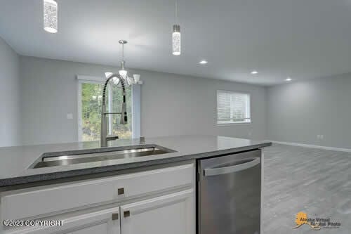 kitchen with a sink, white cabinets, pendant lighting, dishwasher, and open floor plan