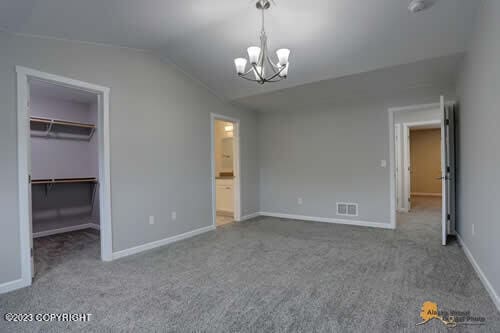 unfurnished bedroom with carpet, visible vents, vaulted ceiling, a spacious closet, and a notable chandelier