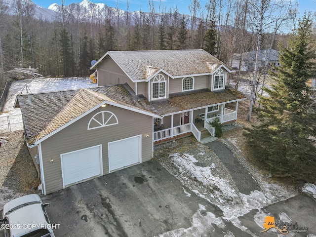 traditional-style home featuring aphalt driveway, covered porch, a view of trees, and a garage