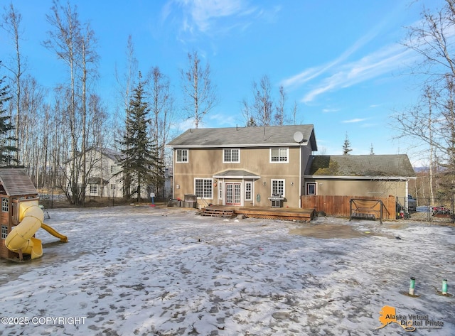 snow covered property with a wooden deck, a playground, and fence