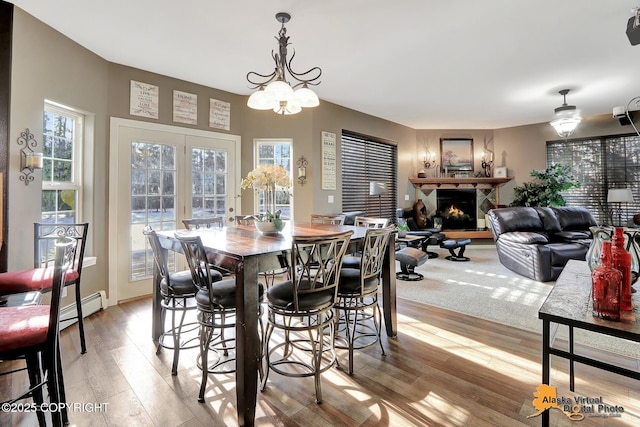 dining area with a baseboard heating unit, a notable chandelier, a warm lit fireplace, and light wood finished floors