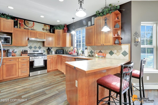 kitchen featuring open shelves, a sink, stainless steel appliances, under cabinet range hood, and baseboard heating