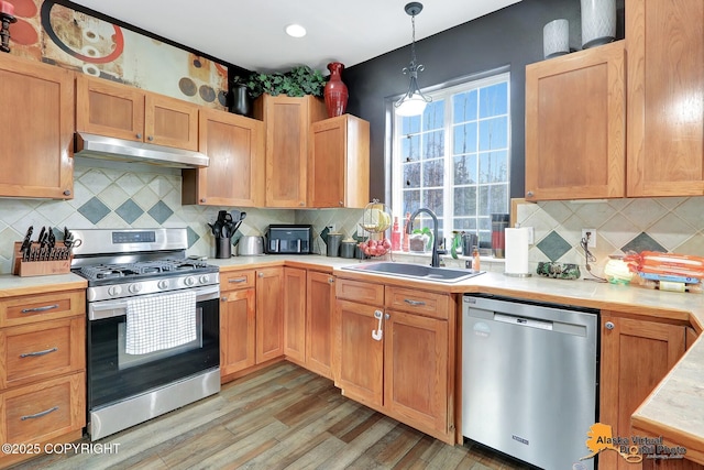 kitchen with under cabinet range hood, a sink, stainless steel appliances, light wood-style floors, and light countertops