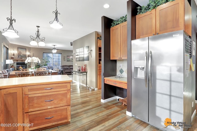 kitchen featuring a glass covered fireplace, open floor plan, light wood-style floors, stainless steel fridge with ice dispenser, and light countertops