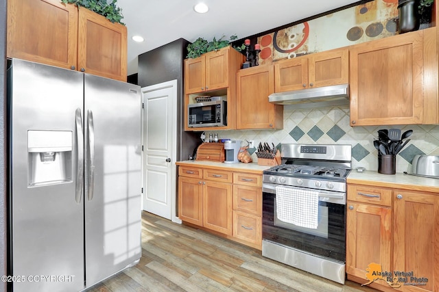 kitchen with under cabinet range hood, light countertops, decorative backsplash, light wood-style floors, and stainless steel appliances