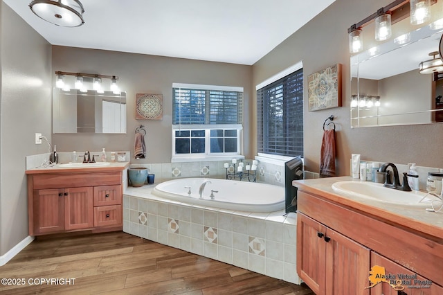 bathroom with two vanities, a bath, wood finished floors, and a sink