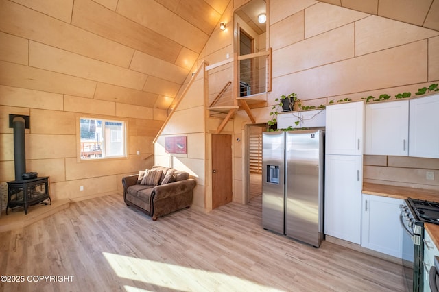 kitchen with high vaulted ceiling, stainless steel appliances, a wood stove, and light wood-type flooring