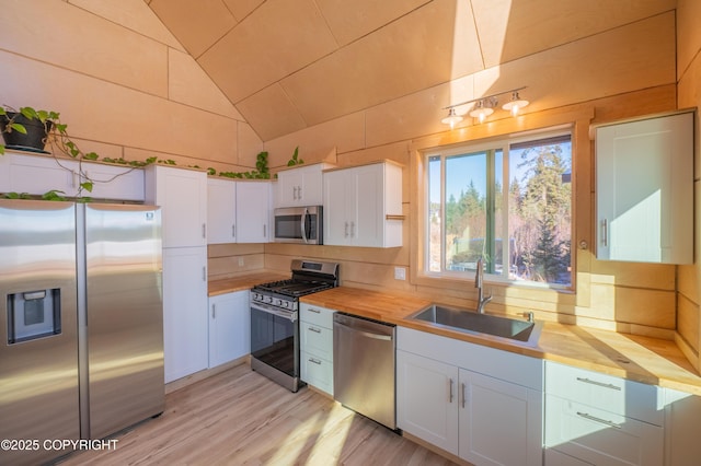 kitchen featuring a sink, butcher block countertops, vaulted ceiling, appliances with stainless steel finishes, and white cabinetry