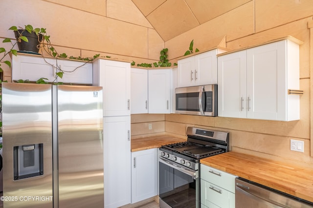 kitchen with lofted ceiling, butcher block countertops, decorative backsplash, white cabinets, and appliances with stainless steel finishes