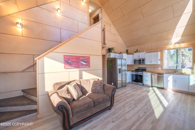 unfurnished living room with a sink, high vaulted ceiling, stairs, and light wood finished floors