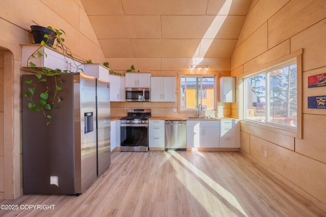 kitchen with a sink, lofted ceiling, appliances with stainless steel finishes, and white cabinetry