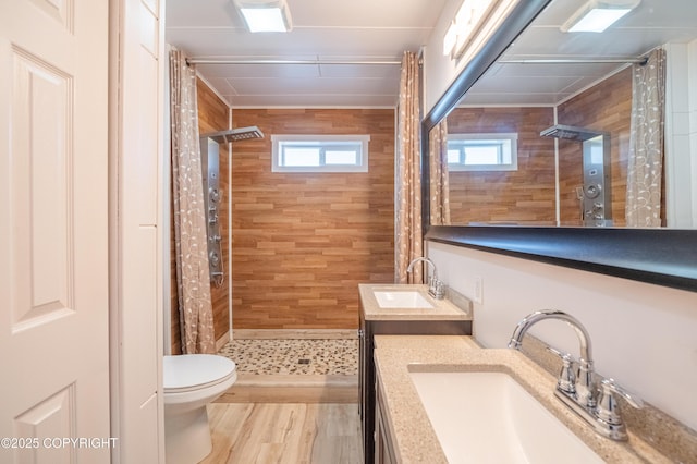 bathroom with toilet, tiled shower, vanity, and wood finished floors