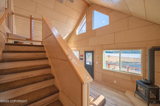 staircase featuring a wealth of natural light, wood walls, a wood stove, and wood finished floors