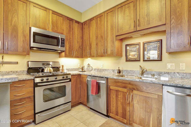 kitchen with brown cabinets, a sink, light stone counters, stainless steel appliances, and light tile patterned floors