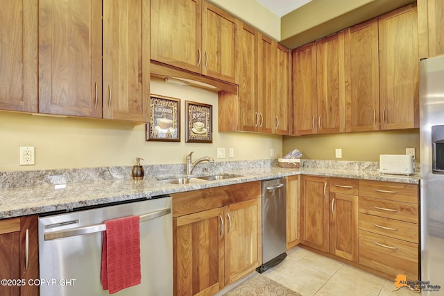 kitchen featuring brown cabinetry, light stone counters, appliances with stainless steel finishes, light tile patterned flooring, and a sink