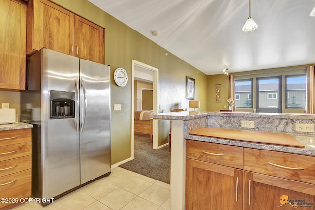 kitchen with baseboards, stainless steel fridge with ice dispenser, light carpet, light tile patterned flooring, and brown cabinetry