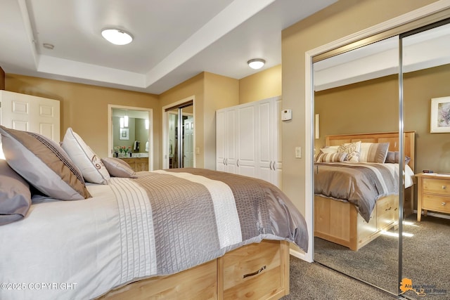 bedroom featuring a raised ceiling, ensuite bathroom, and carpet flooring