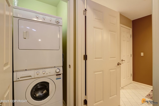 laundry room featuring light tile patterned floors, laundry area, stacked washer and clothes dryer, and baseboards