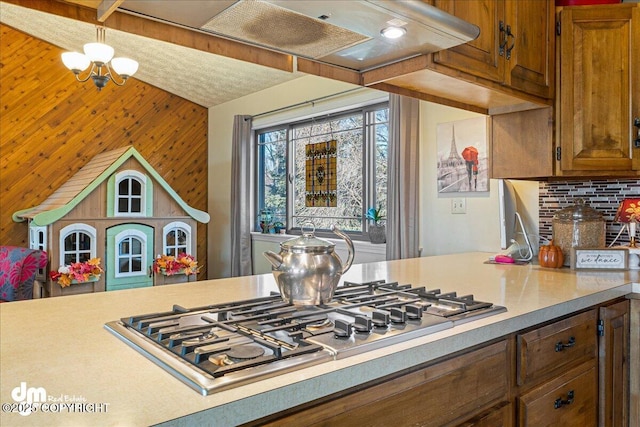 kitchen featuring light countertops, stainless steel gas stovetop, tasteful backsplash, and under cabinet range hood