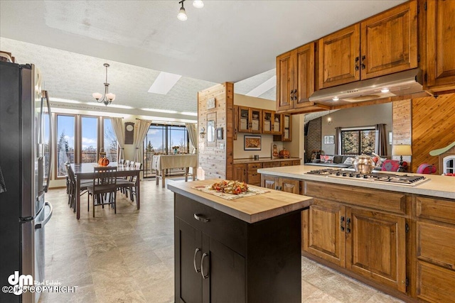 kitchen featuring under cabinet range hood, brown cabinetry, appliances with stainless steel finishes, and a center island