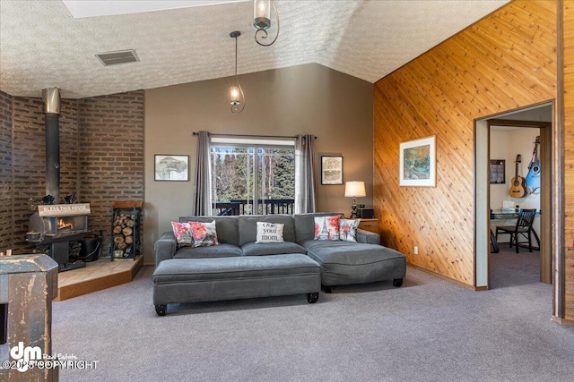 living room with wooden walls, carpet, visible vents, a wood stove, and a textured ceiling