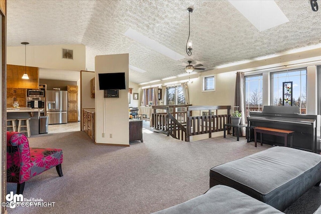 living area with ceiling fan, a textured ceiling, vaulted ceiling with skylight, and light carpet