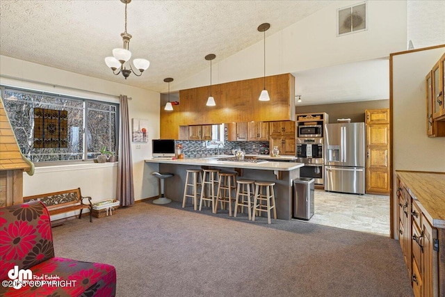 kitchen featuring brown cabinetry, visible vents, a peninsula, stainless steel appliances, and light colored carpet