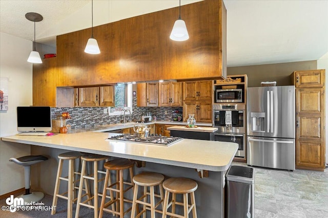 kitchen with appliances with stainless steel finishes, a peninsula, brown cabinetry, light countertops, and decorative backsplash