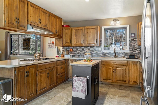 kitchen with brown cabinets, under cabinet range hood, a sink, stainless steel appliances, and light countertops