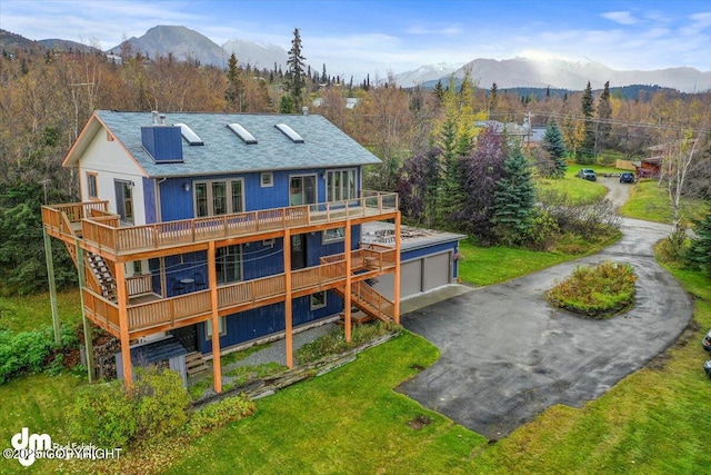 rear view of property with aphalt driveway, stairway, a lawn, a garage, and a deck with mountain view