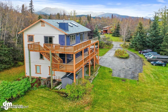 rear view of house featuring a lawn, roof with shingles, a deck with mountain view, and driveway