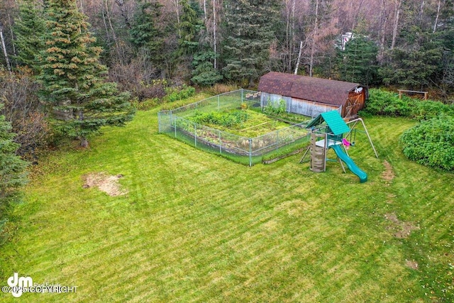 view of yard with fence, a forest view, a garden, an outdoor structure, and a playground