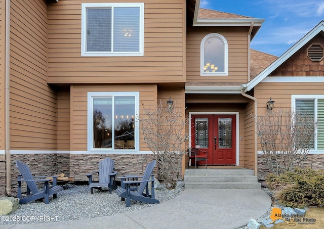 property entrance with french doors, stone siding, and a shingled roof