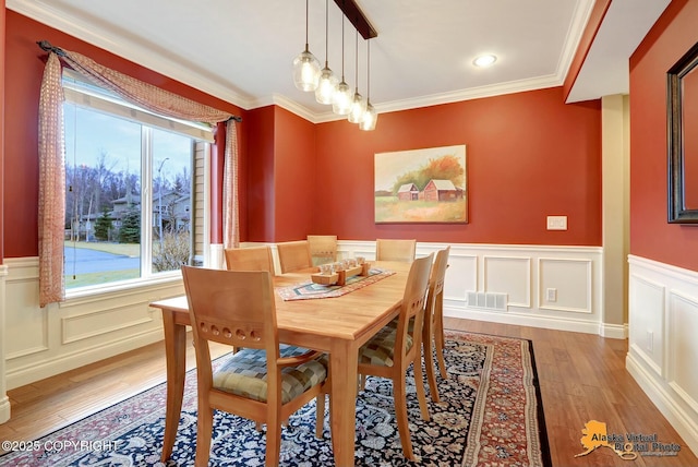 dining room with visible vents, a wainscoted wall, light wood finished floors, crown molding, and a decorative wall