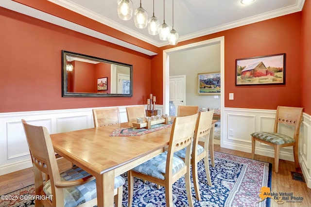 dining room with a wainscoted wall, crown molding, visible vents, and wood finished floors